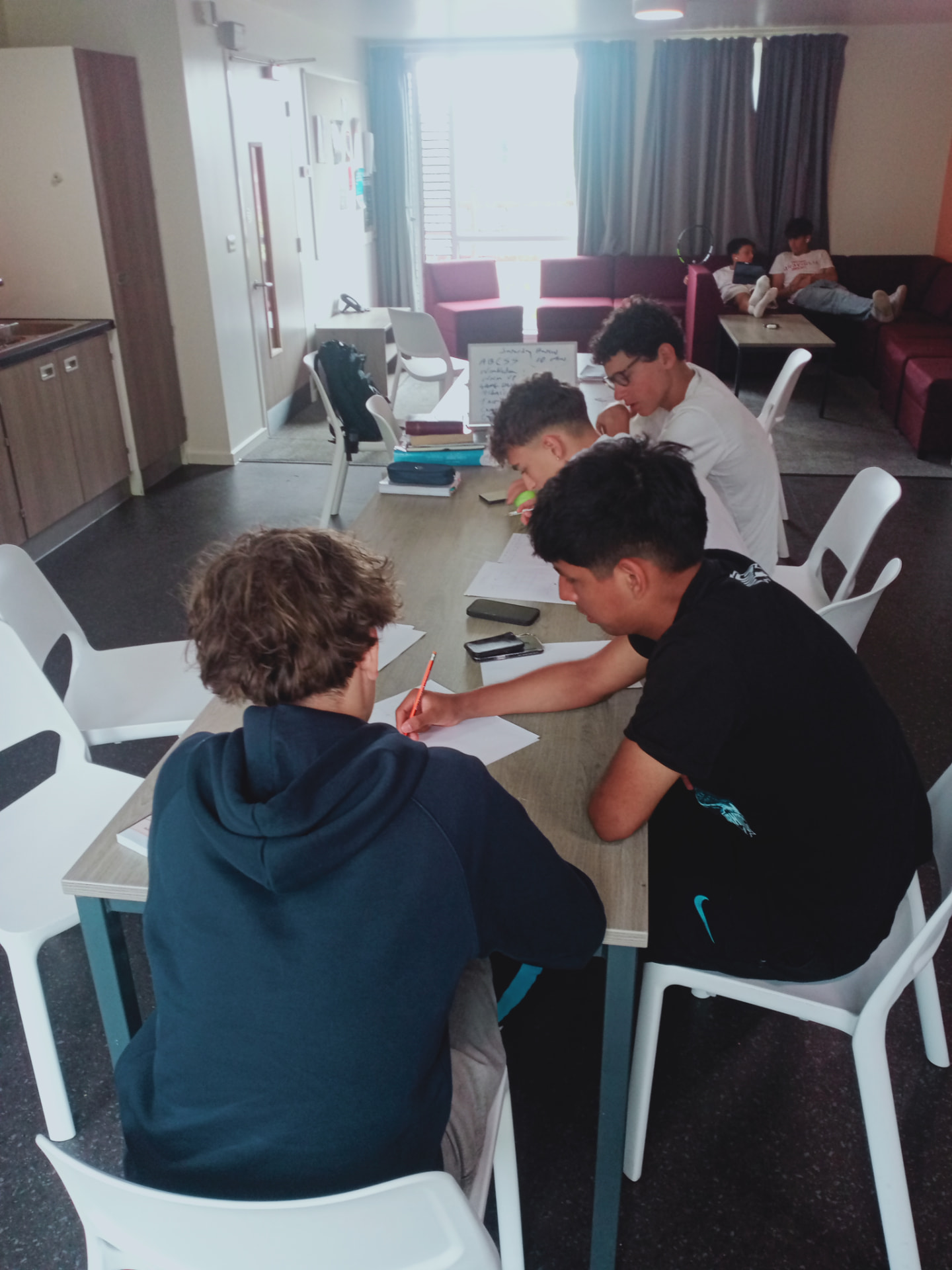 Students working on tennis-related English grammar exercises around a classroom table