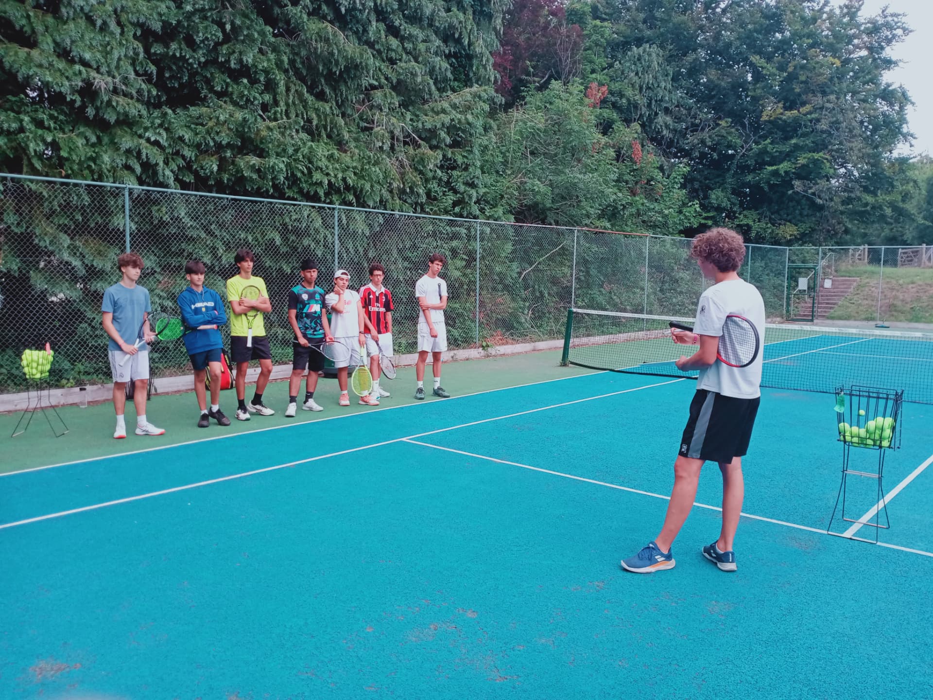 Student delivering a tennis lesson to classmates on court at the University of Sussex English and tennis camp